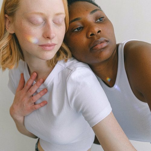 Ava lehnt sich von hinten auf Mayas Schulter, Regenbogen Lichtspiel über Gesichter der beiden Frauen